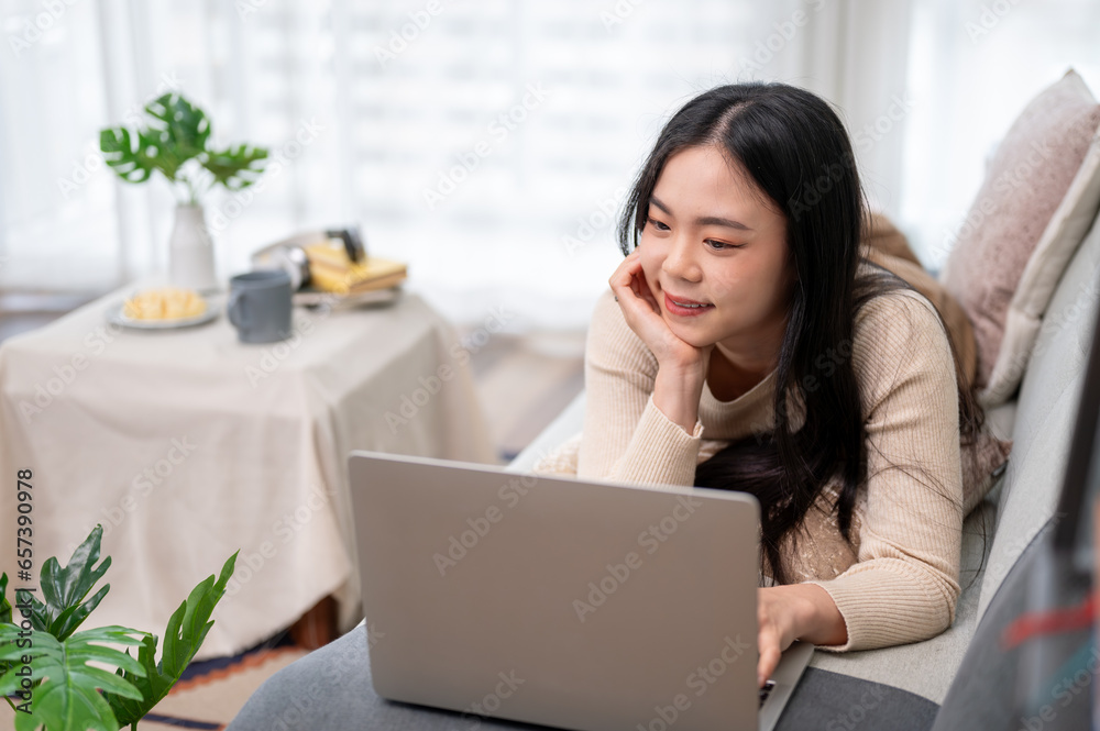 A beautiful Asian woman is using her laptop, watching a movie while lying on a sofa. A beautiful Asian woman is using her laptop, watching a movie while lying on a sofa.