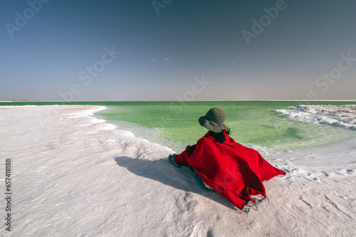 A woman in red dress sitting by green salt lake