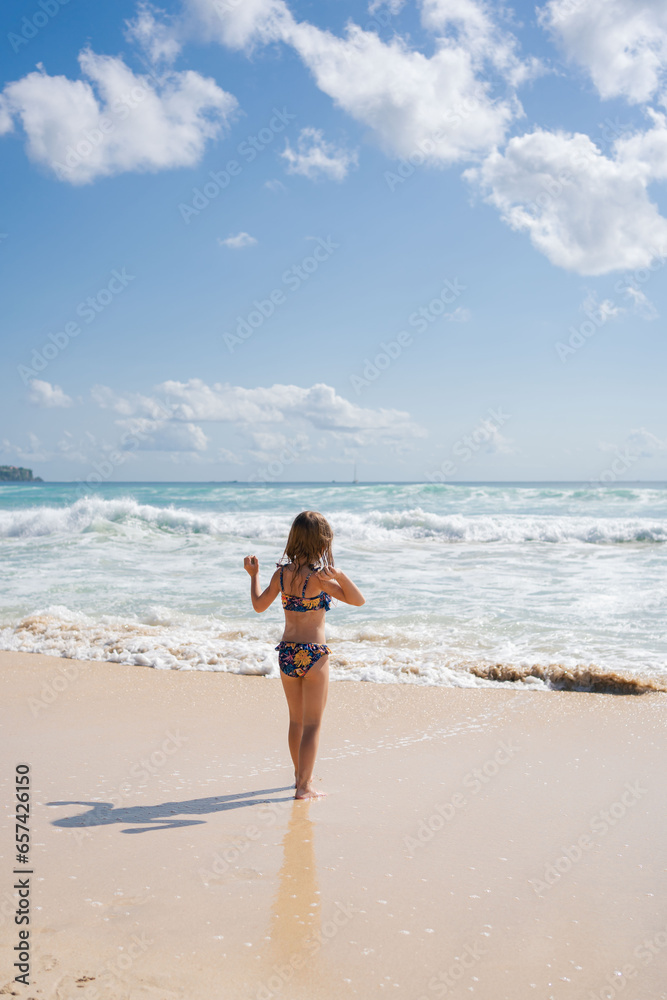 smiling girl child running and playing at the beach while on a family vacation. Playing in the ocean waves having fun and being active.