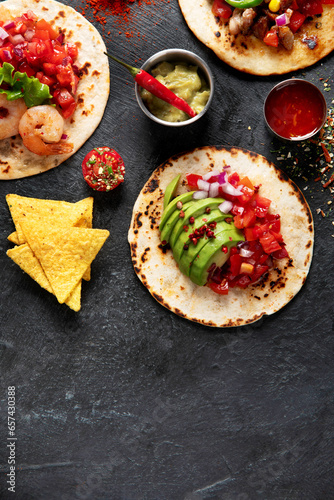 Tacos with salsa, vegetables and avocado on black background