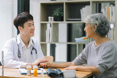 Young Asian male doctor holding hands with a senior patient woman  offering hope and kindness at a modern clinic office.