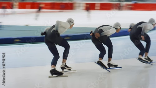 Pan slowmo shot of young polyethnic male group of athlete speed skaters sprinting in skating outfits in indoor ice rink photo