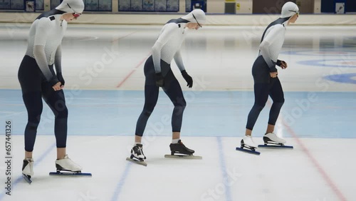 Full slowmo shot of three multiethnic male athlete speed skaters in professional sportswear sprinting off along track in ice rink photo