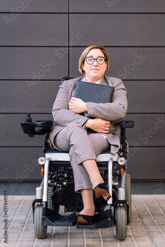 smiling business woman using a wheelchair holding a folder looking at camera, concept of entrepreneurship and diversity, copy space for text photo