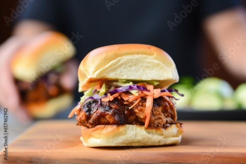 hand holding finishing spicy bbq pork slider against grill backdrop