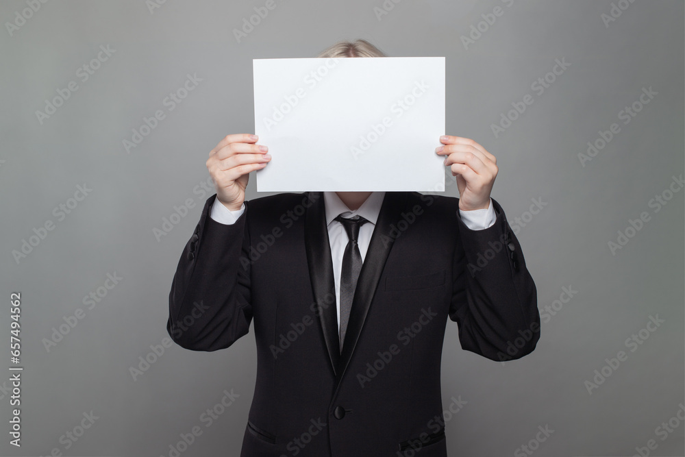 Anonymous businessman hiding his head behind blank empty white paper against gray studio wall background Anonymous businessman hiding his head behind blank empty white paper against gray studio wall background