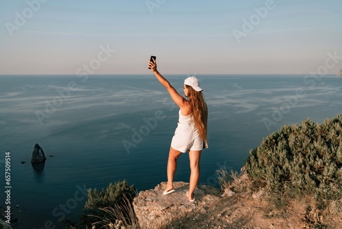 Selfie woman in a cap, white tank top and shorts makes a selfie shot mobile phone post photo social network outdoors on the background of the sea beach people vacation lifestyle travel concept.
