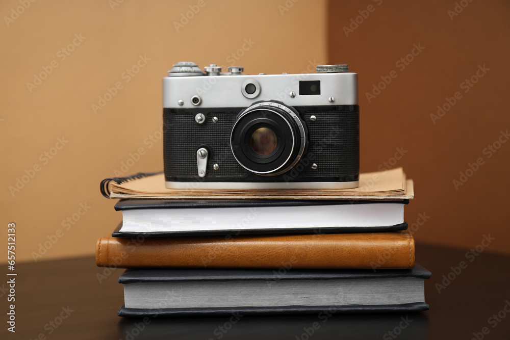 Fototapeta premium Vintage camera and notepads on wooden table on brown background