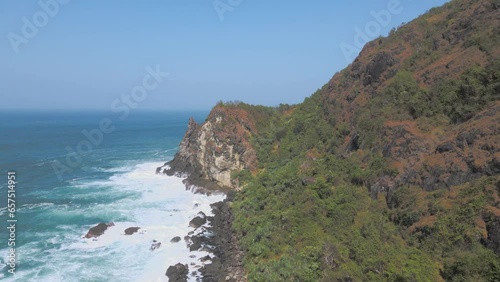 Aerial view of rocky cliff coastline with ocean waves leading up to it. Pengilon hill, The beach is in Gunung Kidul, Indonesia - 4K drone shot photo