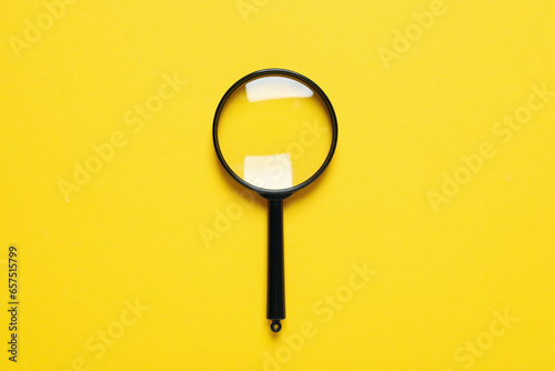 Magnifying glass on yellow background, top view