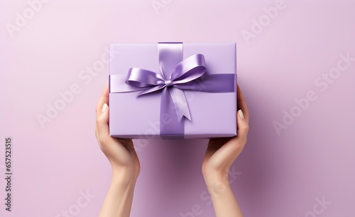 Female hands holding a purple gift box with a bow against pastel background.
