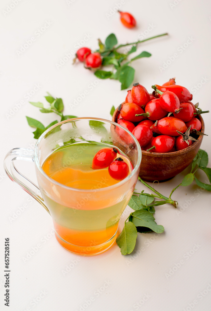 Cup with rosehip drink, bowl with rosehip berries, rosehip branches, berries in a wooden spoon on a light background. Cup with rosehip drink, bowl with rosehip berries, rosehip branches, berries in a wooden spoon on a light background.