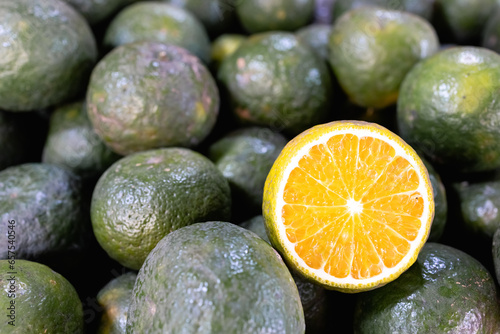 Some fresh limes are whole, and one is cut in half. A mountain of fresh juicy fruits at the fruit market and counter, healthy fruit nutrition. A fresh orange with a green peel and a bright orange core