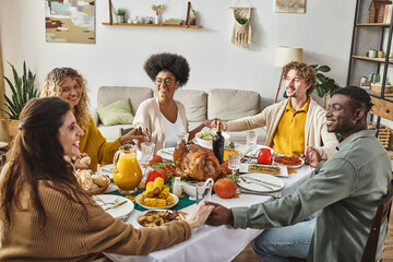 happy multiethnic family sitting at festive table praying and holding hands cheerfully, Thanksgiving