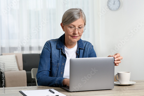 Beautiful senior woman using laptop at wooden table indoors