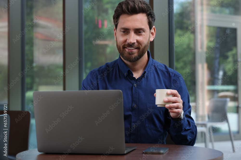 Man with cup of drink using laptop at table in cafe Man with cup of drink using laptop at table in cafe