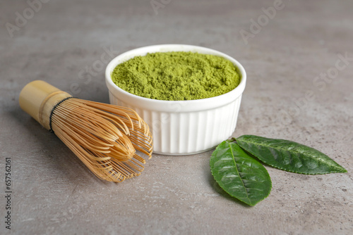 Green matcha powder, bamboo whisk and leaves on light grey table, closeup