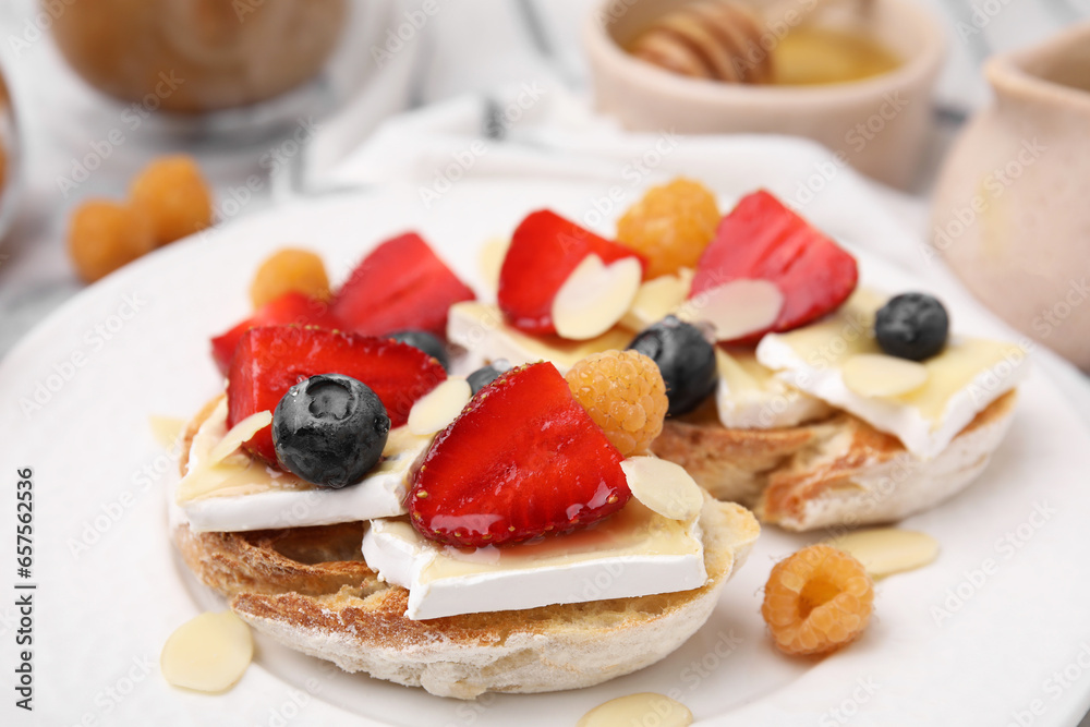 Tasty sandwiches with brie cheese, fresh berries and almond flakes on white plate, closeup