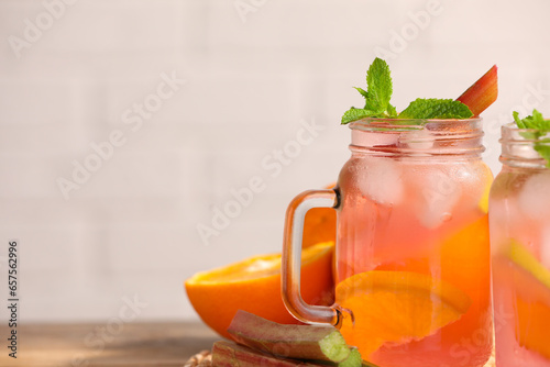 Mason jars of tasty rhubarb cocktail with citrus fruits on table, closeup. Space for text