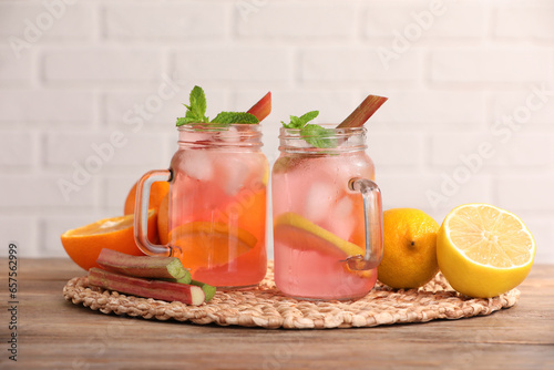 Mason jars of tasty rhubarb cocktail with citrus fruits on wooden table