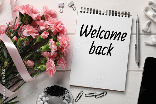 Notebook with phrase Welcome Back, bouquet of flowers and stationery on white wooden table, flat lay photo