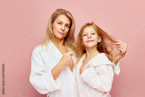 Loving, happy mother and daughter in bathrobes near beauty table looking at camera. Woman and child together care of beauty, health. Cosmetics and wellness of skin.
