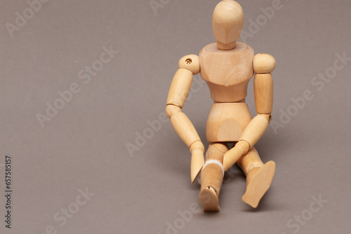 Wooden mvneken sits on the floor with bandaged knee, joint pain concept. photo