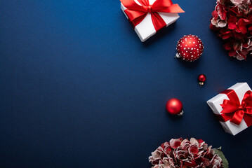 Merry Christmas and Happy Holidays greeting card, frame, banner. New Year. Noel. Red and white Christmas ornaments and gift on blue background top view. Winter xmas holiday theme.