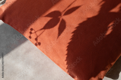 Minimal aesthetic autumn background with orange pillow and natural floral sunlight shadow silhouette of wild grape leaves. Fall cozy home interior decoration, still life photo