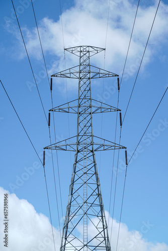 High voltage transmission tower with cable lines against clouds on blue sky background, low angle