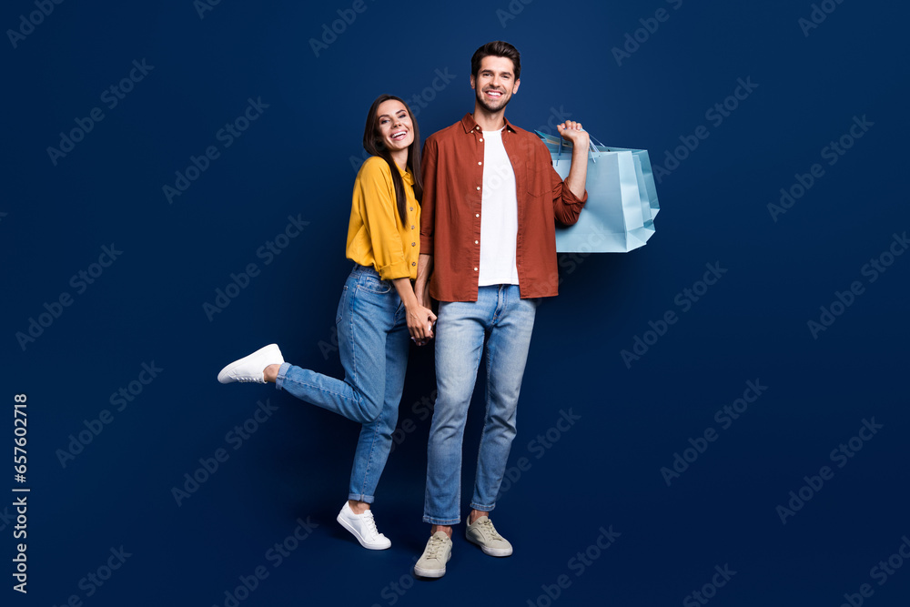 Full length portrait of cheerful funny partners hold hands carry store bags isolated on blue color background