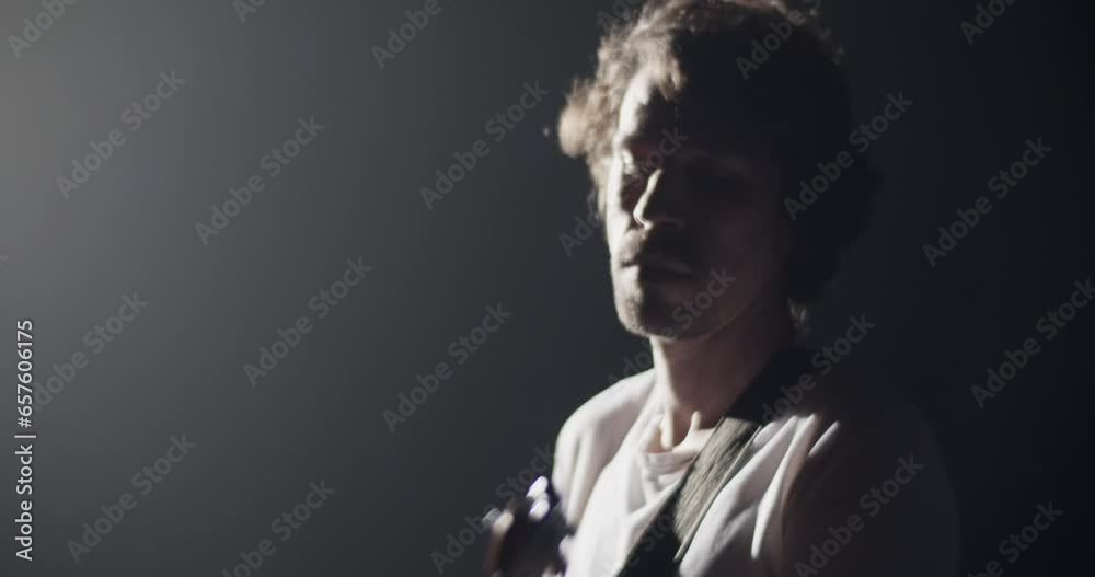 Millennial guitarist playing guitar in studio with spotlight Millennial guitarist playing guitar in studio with spotlight