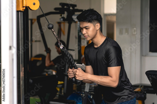 A young handsome asian man does a set of tricep pushdowns at a hardcore gym.