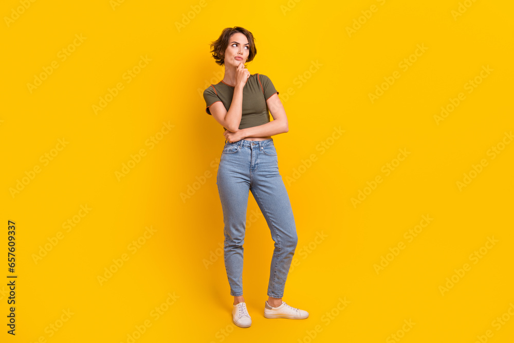Photo of adorable confused unsure woman wear trendy t-shirt jeans thoughtfully look at empty space isolated on yellow color background Photo of adorable confused unsure woman wear trendy t-shirt jeans thoughtfully look at empty space isolated on yellow color background