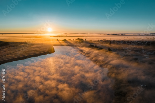 Fog billows from lake in early autumn morning. Sun on horizon in blue sky