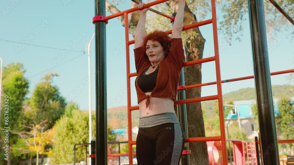 Adult Caucasian woman is hanging on horizontal bar and doing crunches for core. Exercises - Swedish stairs, lifting legs. Slow motion. Concept of healthy lifestyle and sport Adult Caucasian woman is hanging on horizontal bar and doing crunches for core. Exercises - Swedish stairs, lifting legs. Slow motion. Concept of healthy lifestyle and sport