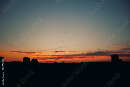 Cloudy red-blue sunset over dark silhouettes of city buildings, top view. Evening view.