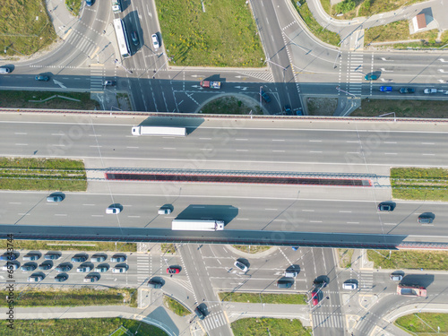 Aerial top view of highway junction interchange road. Drone view of the elevated road, traffic junctions, and green garden. Transport trucks and cars driving on highway. Infrastructure in modern city.