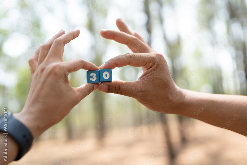 The hands of a man and woman hold a blue number box showing the number three and zero. The hands of a man and woman hold a blue number box showing the number three and zero.