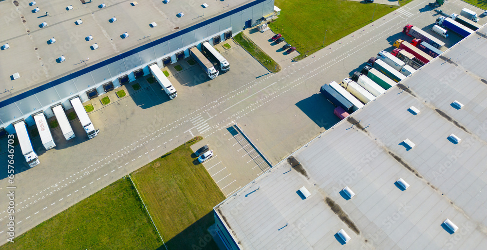 Aerial view of goods warehouse. Logistics center in industrial city zone from above. Aerial view of trucks loading at logistic center - obrazy, fototapety, plakaty 