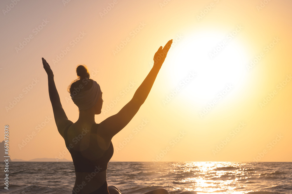 Free happy woman raises her hands and looks at the sun, rear side view. In the background, dawn, greeting the sun during yoga or meditation