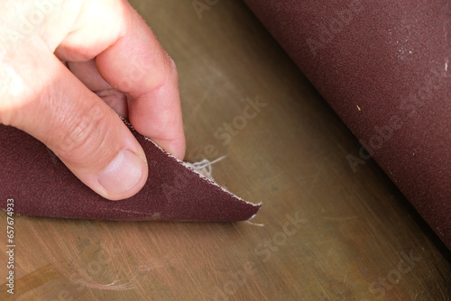 Tablou pe pânză Human hand with sandpaper on a copper background