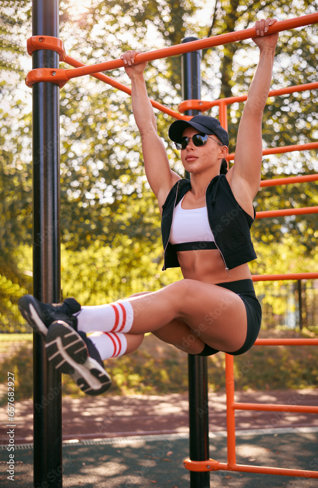 Beautiful young fitness girl is warming up at the stadium before training. Attractive slender brunette in a tracksuit, black cap and sunglasses.