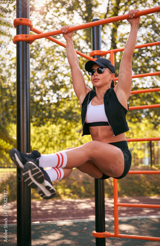 Beautiful young fitness girl is warming up at the stadium before training. Attractive slender brunette in a tracksuit, black cap and sunglasses.