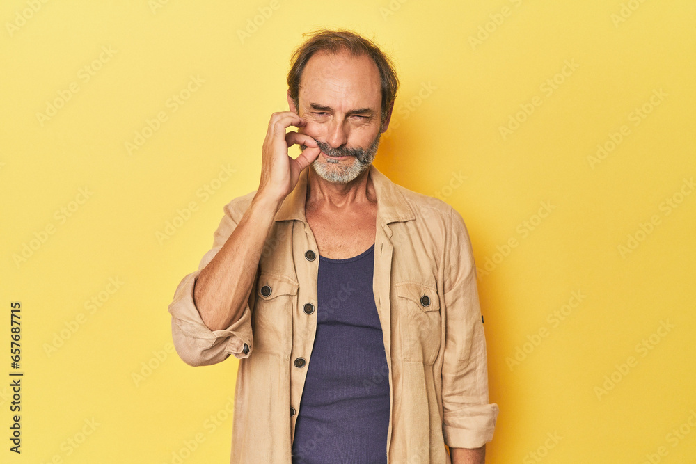 Caucasian middle-aged man in yellow studio with fingers on lips keeping a secret. Caucasian middle-aged man in yellow studio with fingers on lips keeping a secret.