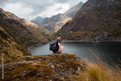 Un turista con mochila sentado con brazos abiertos en una roca a orillas de una laguna (Laguna Linda, Pachitea, Perú),paz,concepto de viajar,turismo