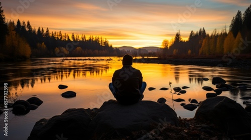 Silhouette of person meditating by tranquil lake at sunset.