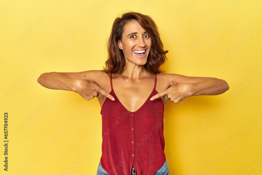 Middle-aged woman on a yellow backdrop surprised pointing with finger, smiling broadly. Middle-aged woman on a yellow backdrop surprised pointing with finger, smiling broadly.