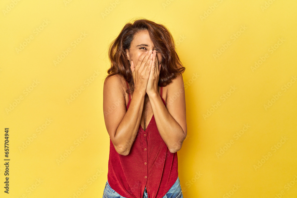 Middle-aged woman on a yellow backdrop laughing about something, covering mouth with hands. Middle-aged woman on a yellow backdrop laughing about something, covering mouth with hands.