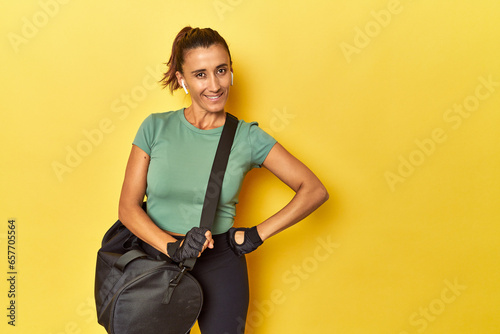 фотографія Middle aged sportswoman with gym backpack on yellow backdrop